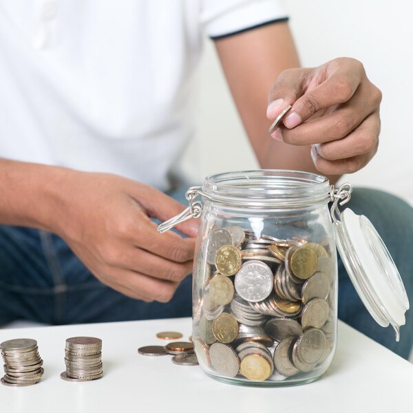 midsection-man-putting-coins-jar-table-home